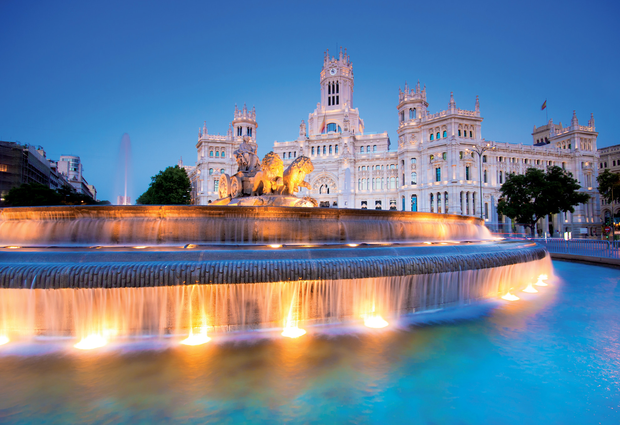A view of the Palacio de Comunicaciones in Plaza de la Cibeles, Madrid at dusk behind a large water feature
